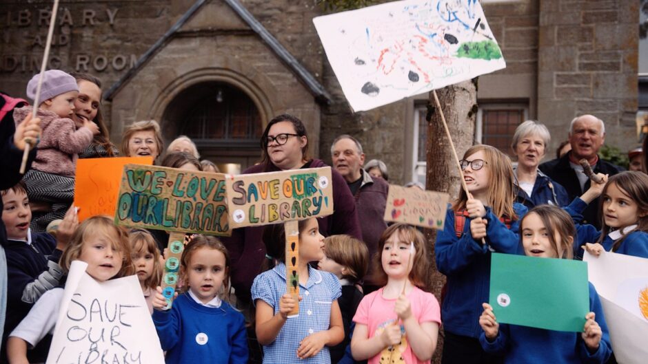 Group of adults and children with Save Our Library placards outside Birnam Library