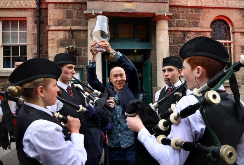 McIlvanney Prize winner, Chris Brookmyre holds his trophy up proudly surrounded by the pipe band. 