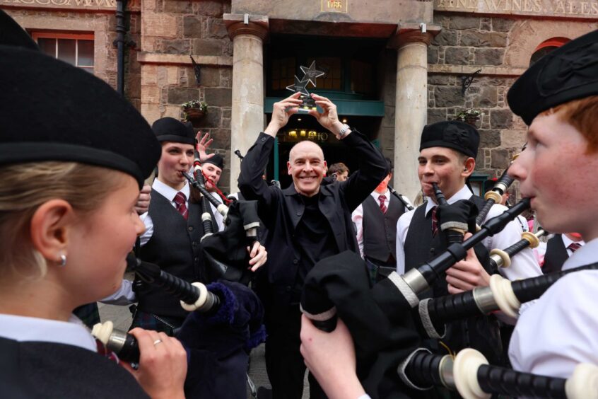 Debut Prize winner, Alan Gaw holds his trophy up proudly surrounded by the pipe band. 