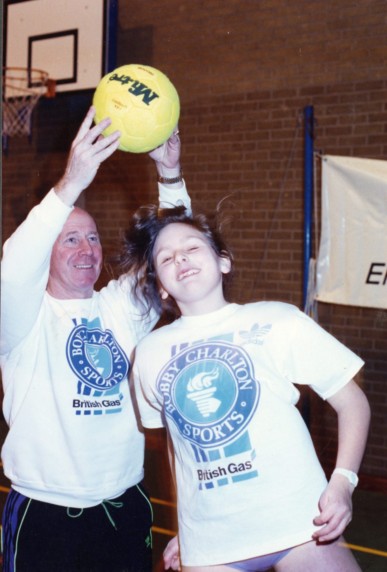 Bobby Charlton holds a ball as a young girl jumps to head it