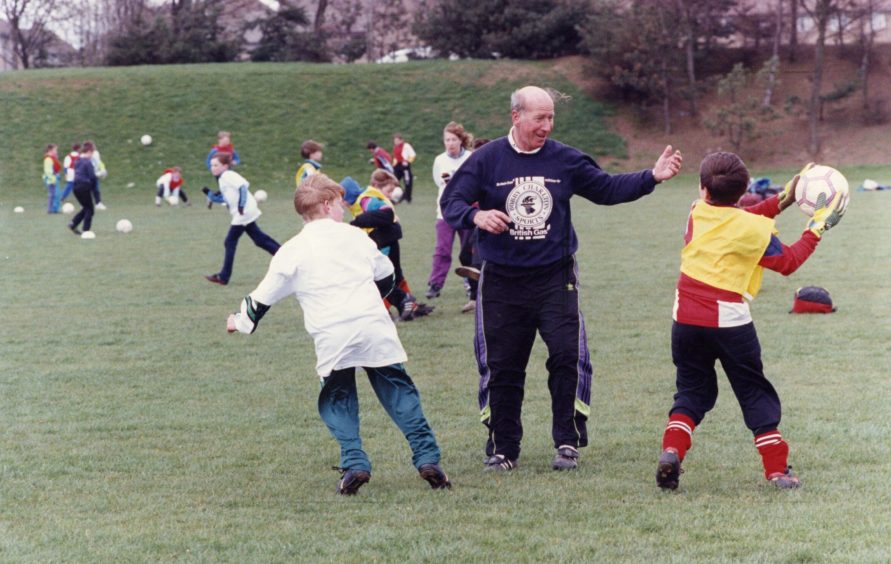 Sir Bobby coaches two boys at the Gardyne campus in Dundee in April 1991, while other youngsters do drills in the background. 