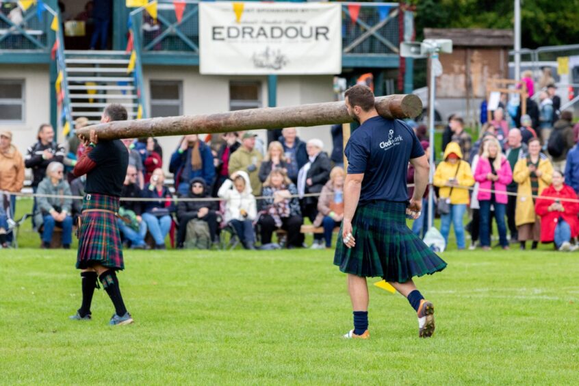 2 men carry the caber into the games arena. 