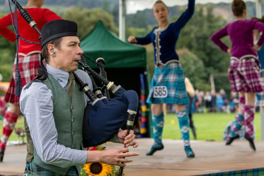 A piper accompanies the highland dancers. 