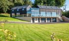 the lawn leading up to a large, modern home with a wraparound balcony