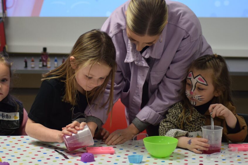 Image shows two girls at a party at Dundee Science Centre. The girls are getting involved in a science session with one of the adult leaders.