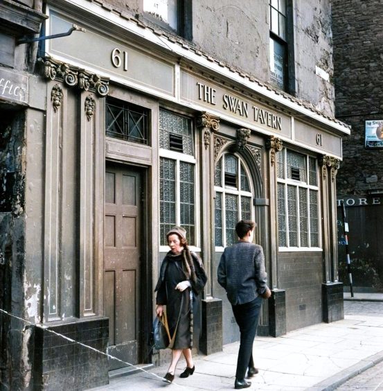 two people walk past The Swan Tavern, which sits ready for demolition in October 1963.