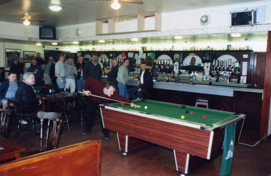 People seated and standing, with a man preparing to play a shot at the pool table. 