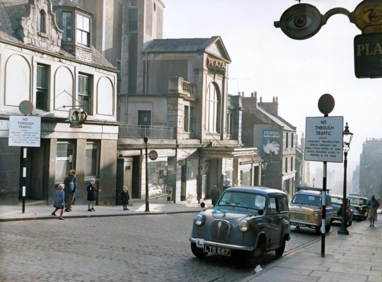 The Hilltown in November 1960, as a family walks past the Windmill bar and cars are parked on the road