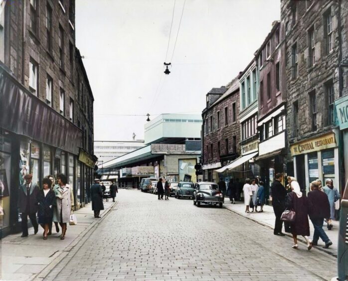 people walking outside shops in a cobbled street in the old Overgate. 