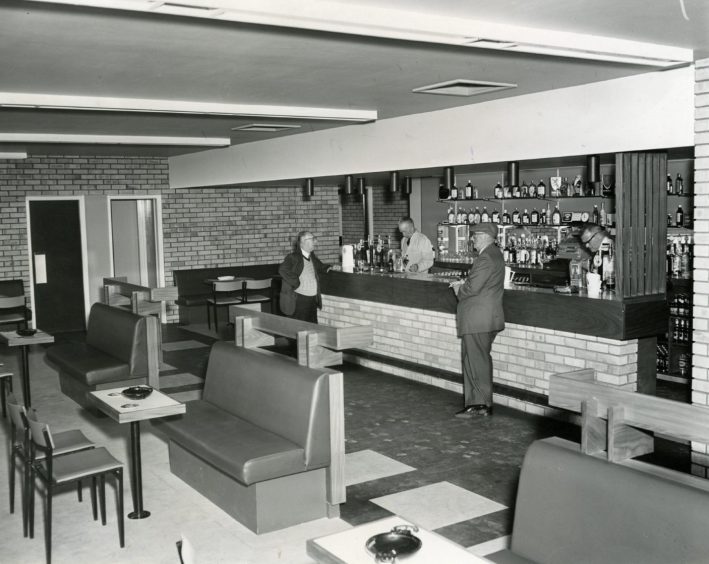 Two men stand at the bar, with the barman behind it, in the The Bayview Bar 