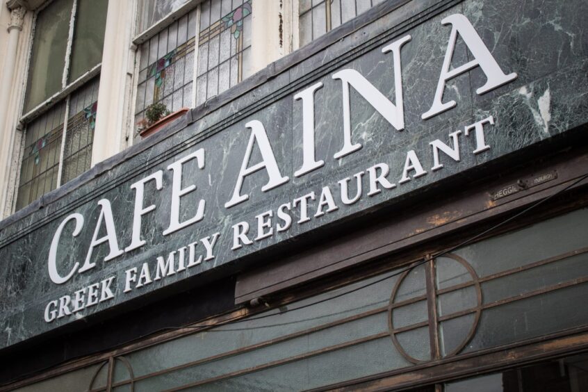 Close-up of marble-effect Cafe Aina sign in Stirling with the words 'Greek family restaurant' underneath.