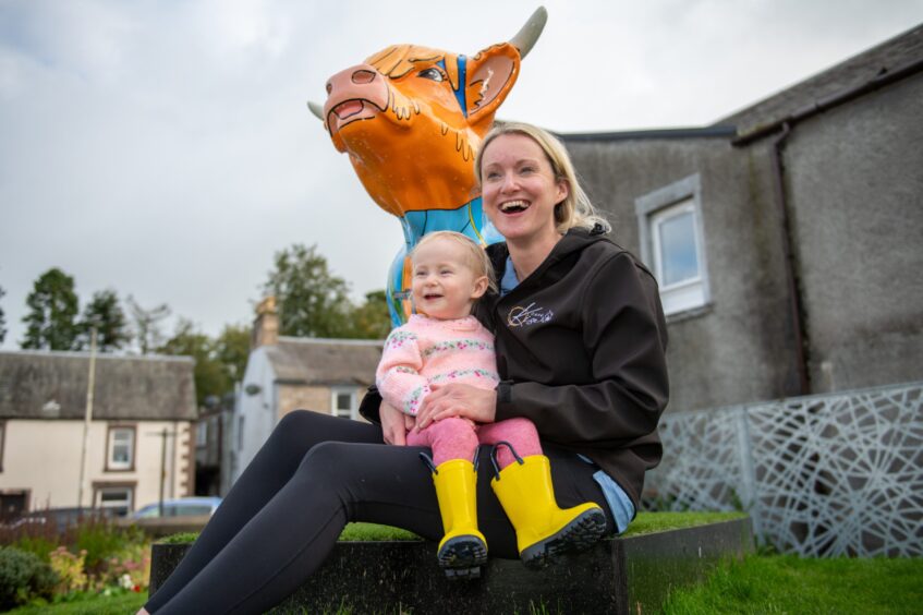 Woman with small child, both smiling broadly next to a painted Highland cow sculpture