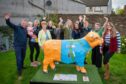 Group of people standing round highland cow sculpture in Auchterarder