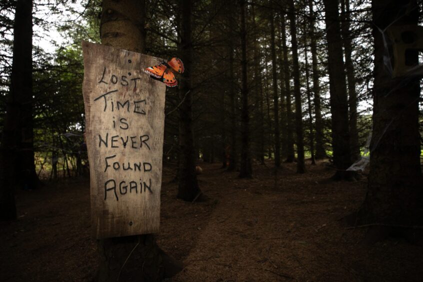 Image shows: a spooky sign at Brechin Castle's Halloween trail. A sign reading Lost Time is Never Found Again sits by the entrance to a dark wood.