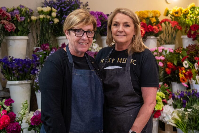 Lynn Smith and Lorna Davies smiling in front of buckets of flowers inside their florist shop