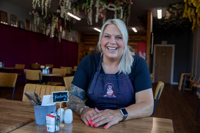 Smiling owner Kelly Duncan sitting at a table in The Madhouse Bakery in Glenrothes.