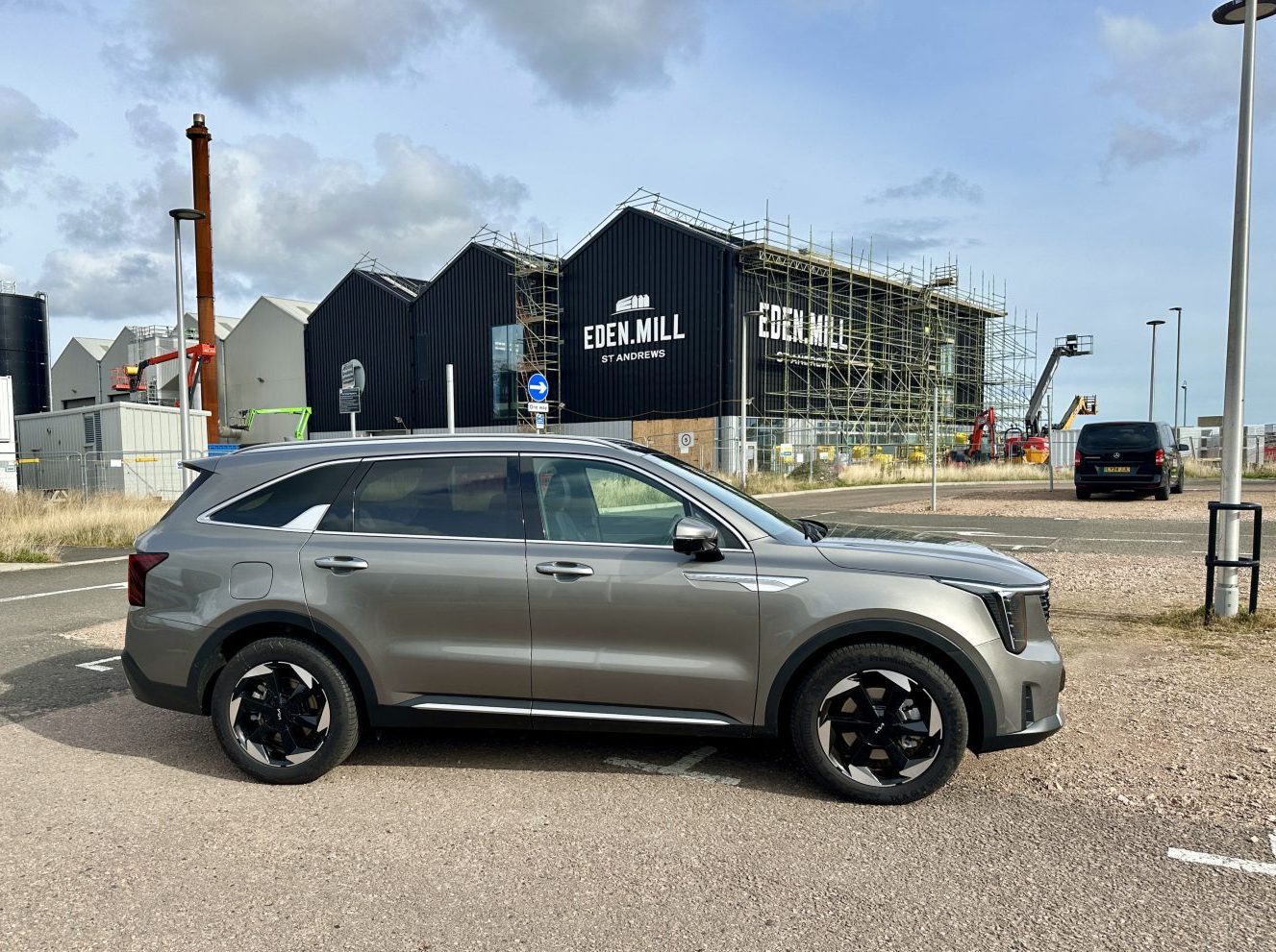 A silver Kia Sorento parked on a gravel patch with warehouses in the background.