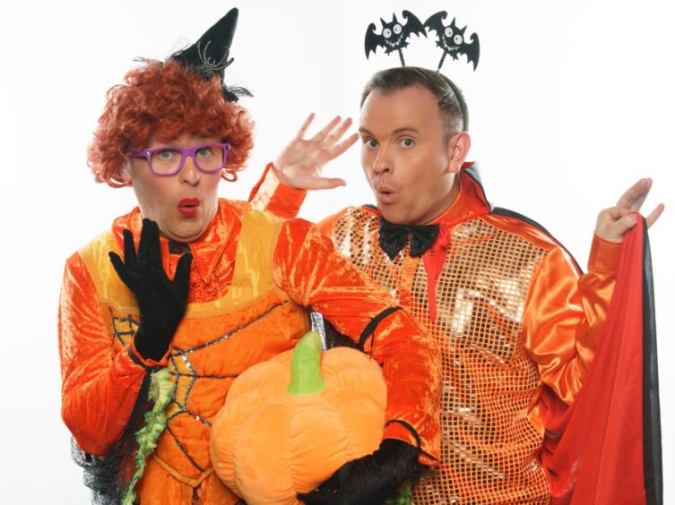 Image shows: children's theatre entertainers The McDougalls dressed in costume for their Halloween show. The two actors are dressed in orange with Halloween accessories including bat headbands, witches hat and a pumpkin.