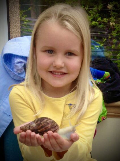 Ruby Stewart with big smile and long hair holding a giant snail to the camera