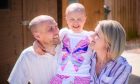 Ruby Stewart smiling in the sunshine with her parents on either side