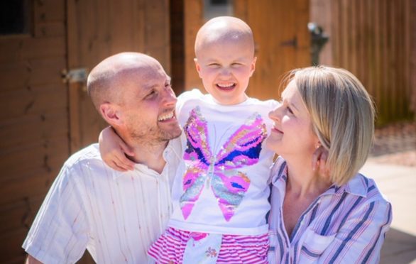 Ruby Stewart smiling in the sunshine with her parents on either side