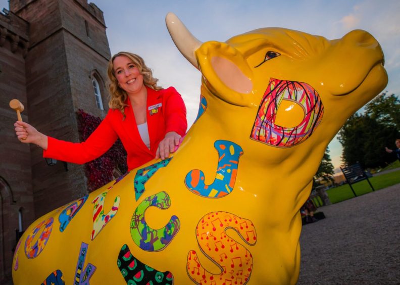 Hayley Smith standing next to yellow painted cow sculpture outside Scone Palace