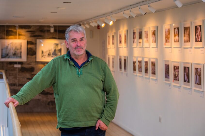 Munro Gauld standing in front of row of photos at Birnam Arts