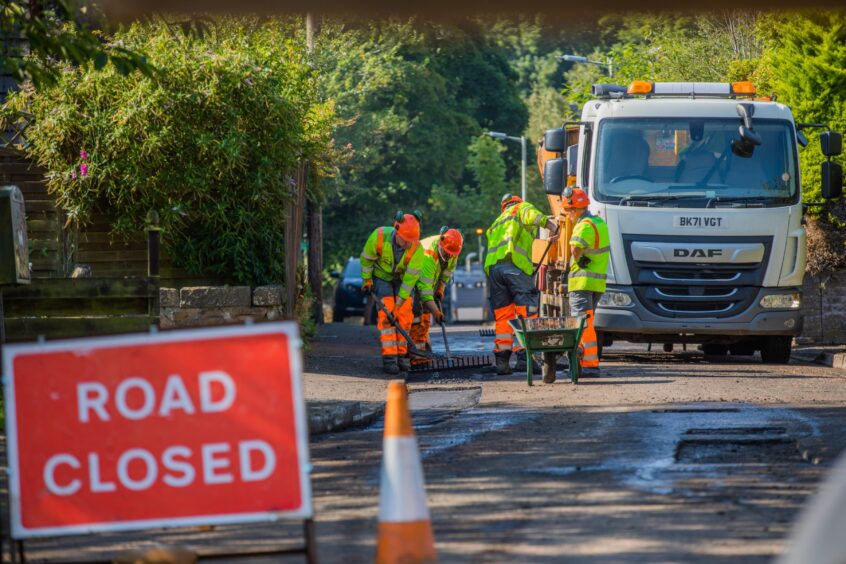 Workers fixing potholes by hand in Rattray, Perthshire, in front of Road Closed sign