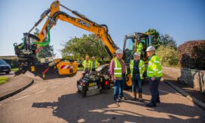 Pothole machine in Rattray, with three councillors in hard hats standing in front of it.