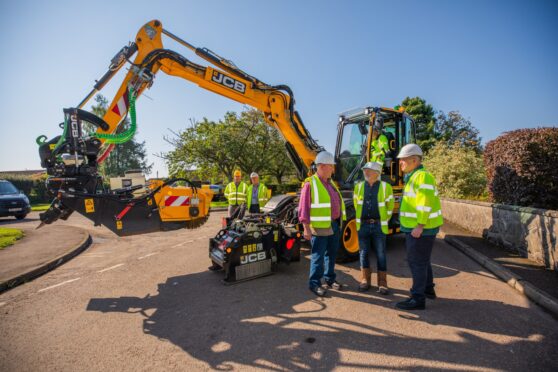 Pothole machine in Rattray, with three councillors in hard hats standing in front of it.