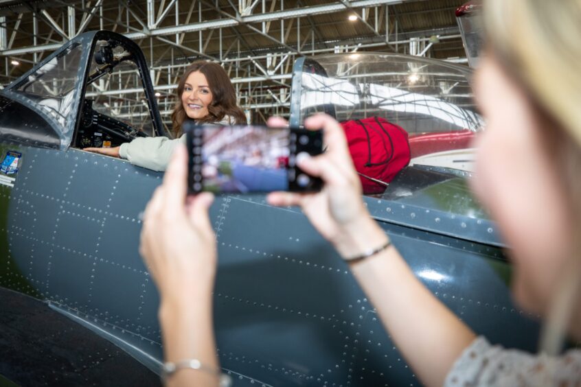 Rachel Coull smiling seated in cockpit while another woman takes a photo