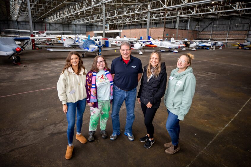 Jim Lachendro, surrounded by four women inside hangar full of planes at Perth airport