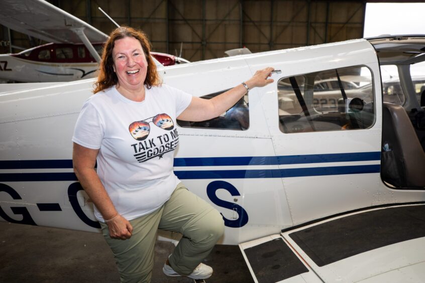 Woman in 'talk to me goose' T shirt standing next to small plane in hangar at Perth airport