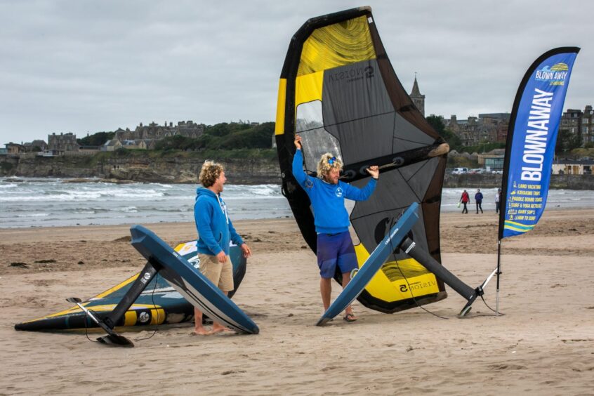 Image shows: Guy and Jamie of Blown Away setting up their wingfoiling kit at West Sands Beach, St Andrews. There are two foils or surf boards with long fins in the foreground and Guy is holding one of the inflatable wings aloft.