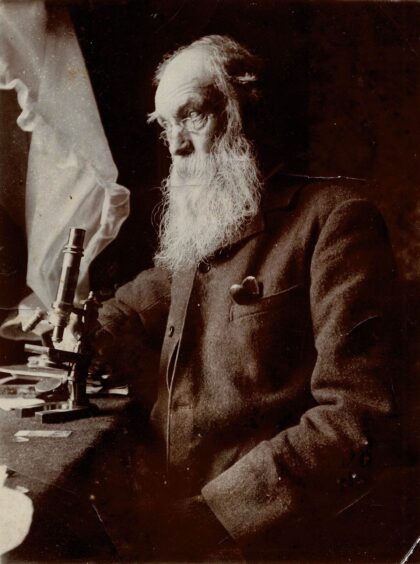 Charles MacIntosh with long white beard seated at microscope