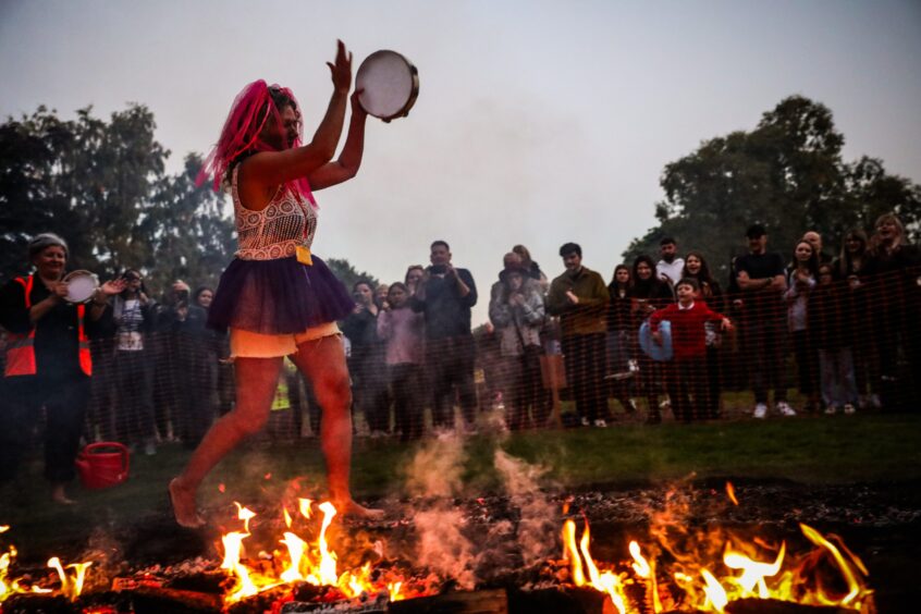 Woman walking across burning coals barefoot banging a tambourine