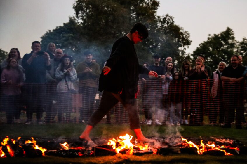 Woman walking barefoot across burning coals in front of cheering crowd