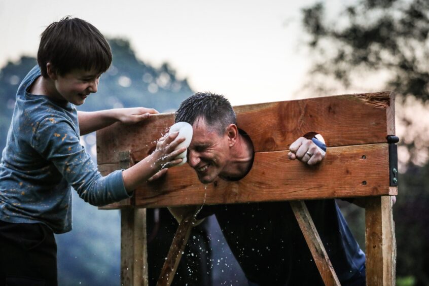 Man in stocks being pelted with wet sponge by young boy