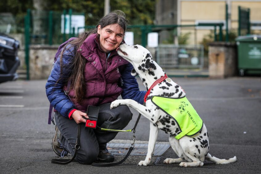 Sonja Shepherd kneeling beside dalmation dog as it licks her face