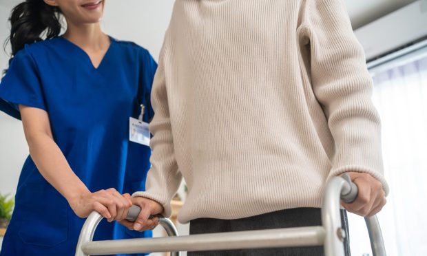 Asian senior elderly man patient doing physical therapy with caregiver. Attractive specialist carer women help and support older mature male practice walking slowly with walker at nursing home care.; Shutterstock ID 2147078197; purchase_order: ; job: