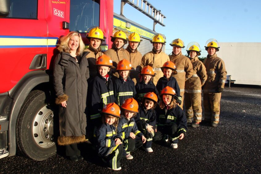 a fire crew and children dressed in firefighters' gear beside a fire engine