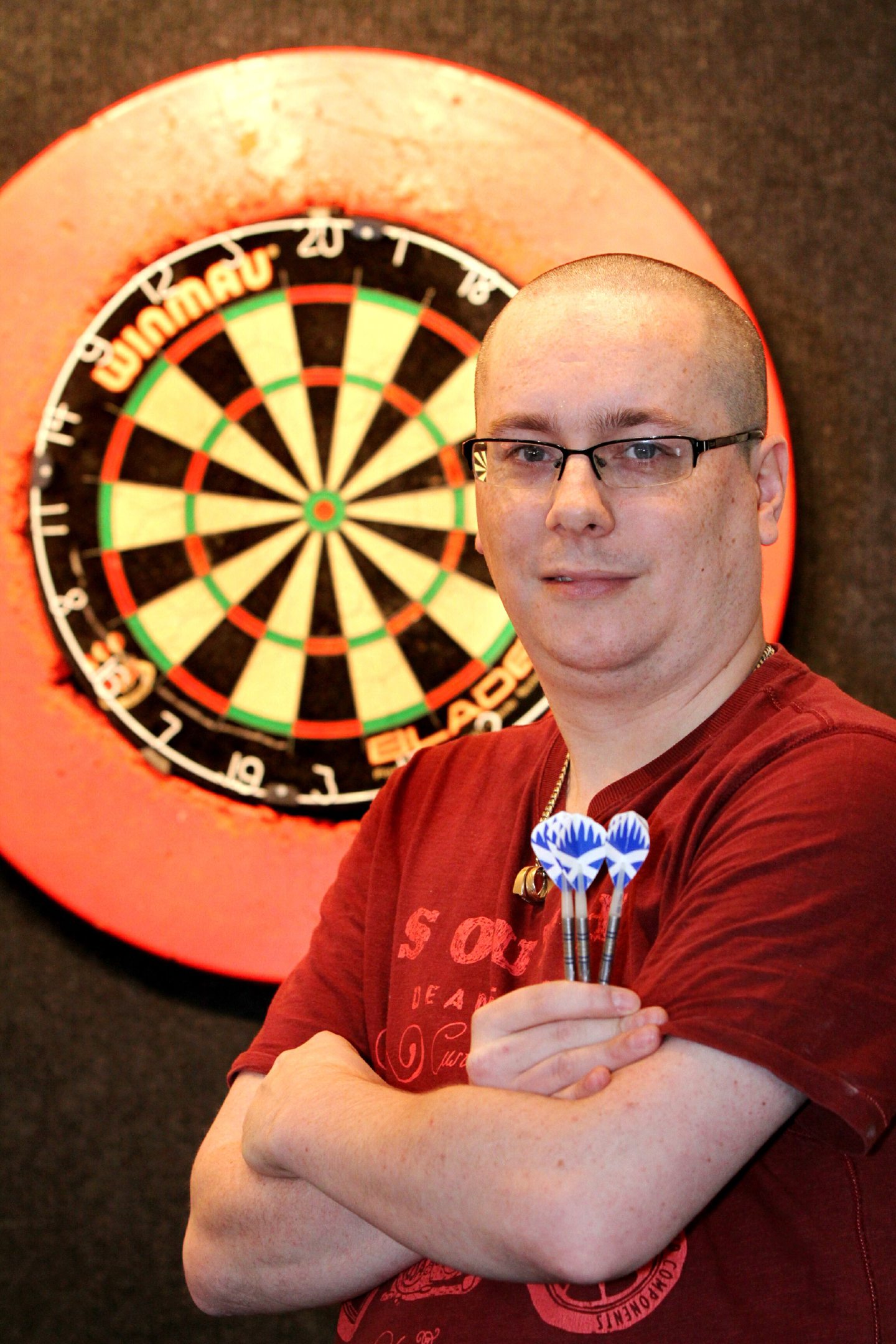 Paul Coughlin , barman and darts player at the Harlequins pub in Dundee, standing before a dart board and holding three darts.