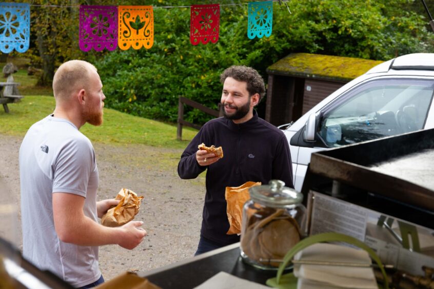 Two male customers chatting and enjoying their quesadillas outside the Zacatecas food truck at Crombie Park.