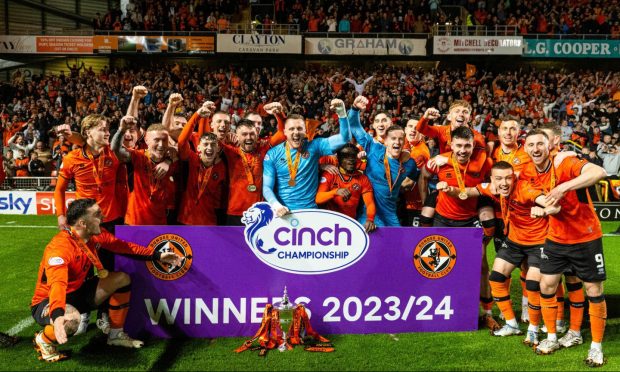 Dundee United players gather around a hoarding and the trophy to celebrate their promotion at Tannadice