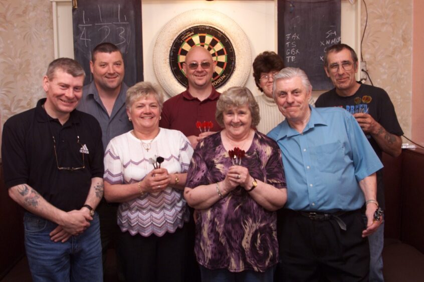 Smiling faces all round as the darts players pose before the dart board before the fundraising drive.