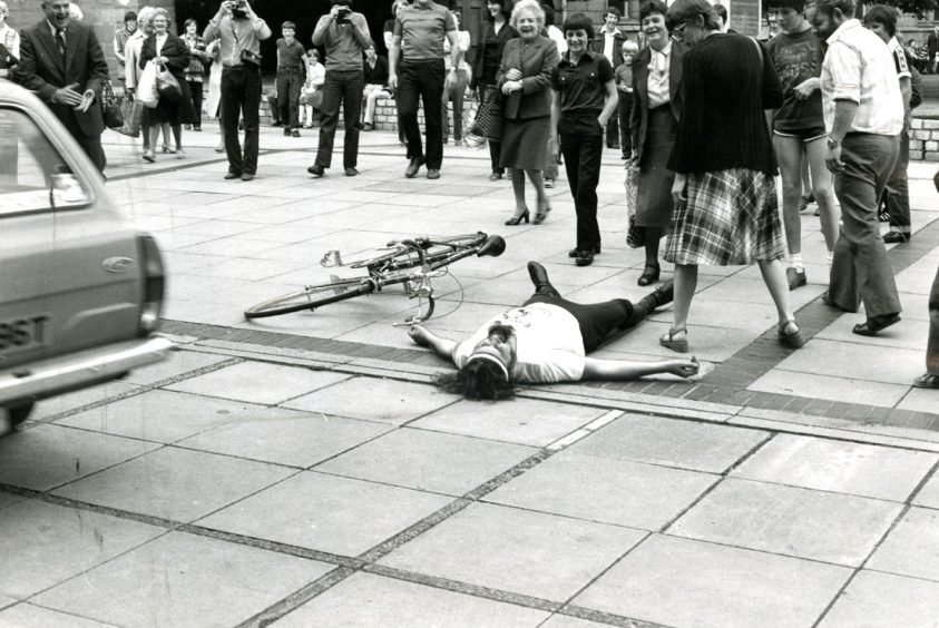 Billy Connolly, lying beside his bike as people look on, stages a mock collapse on his arrival in Dundee. 