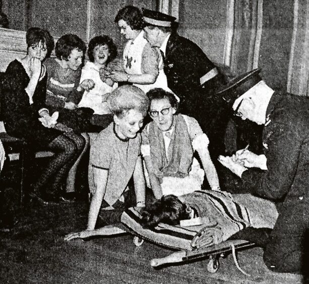 a woman on a stretcher while medical staff talk to three other woman backstage