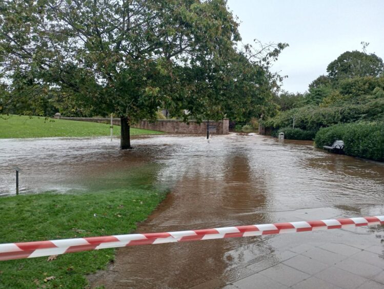 filthy water pouring across grass from open space in flood defences