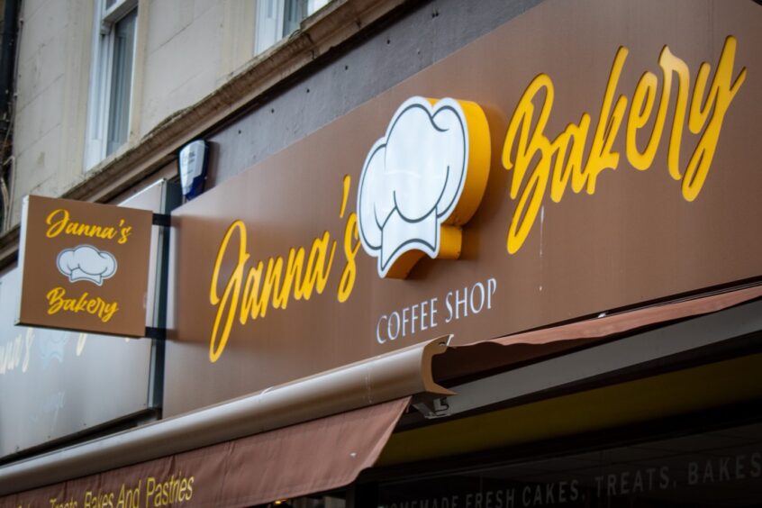 Close-up of brown Janna's Bakery sign on exterior of cafe in Stirling, with yellow writing.