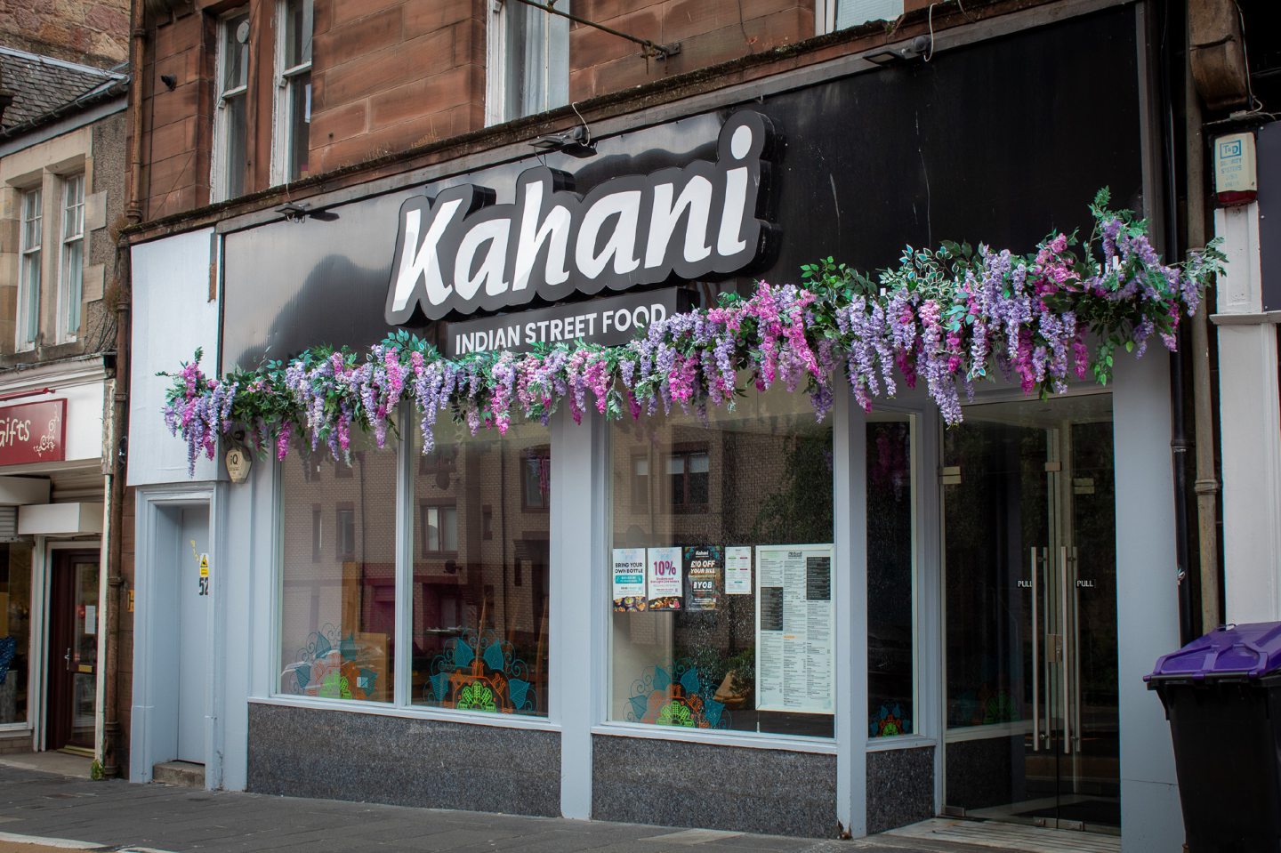 Exterior of Kahani Indian street food with colourful purple flowers under the sign